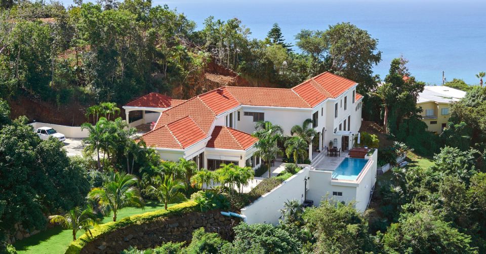 A modern luxury house with palm trees, large windows, and a poolside deck under a clear blue tropical sky.